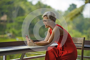 Attractive and relaxed 40s or 50s Asian woman with grey hair and stylish red dress using social media on inernet mobile phone at