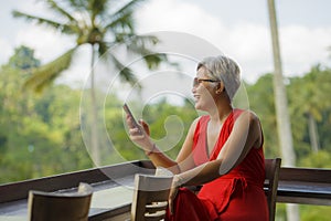 Attractive and relaxed 40s or 50s Asian woman with grey hair and stylish red dress using social media on inernet mobile phone at