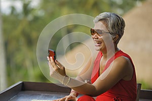 Attractive and relaxed 40s or 50s Asian woman with grey hair and stylish red dress using social media on inernet mobile phone at