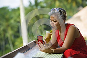 Attractive and relaxed Asian woman with grey hair and stylish red dress using social media on inernet mobile phone at beautiful