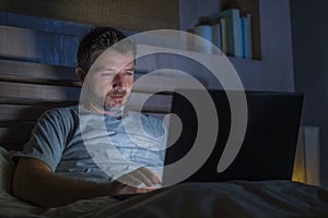 Attractive and relaxed internet addict man networking concentrated late at night on bed with laptop computer in social media