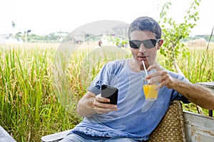 Attractive 30s Caucasian man smiling happy and relaxed sitting at rice field coffee shop in Asia holiday trip using internet on mo