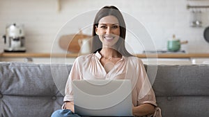 Woman sitting on couch holding computer looking at camera