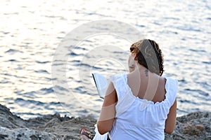 Attractive 40s woman sitting alone on the beach reading a book