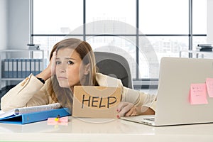 Attractive sad and desperate business woman suffering stress at office laptop computer desk holding help sign