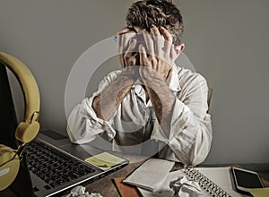 Attractive sad and desperate man in lose necktie looking messy and depressed working at laptop computer desk in business office pr