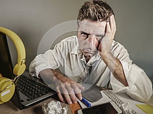 Attractive sad and desperate man in lose necktie looking messy and depressed working at laptop computer desk in business office pr