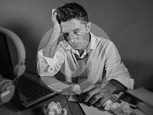 Attractive sad and desperate man in lose necktie looking messy and depressed working at laptop computer desk in business office pr
