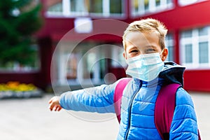 Attractive schoolboy in protective mask standing outdoor excited child points finger at school close up