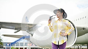 An attractive senior Asian lady in a summer outfit stands at the airport