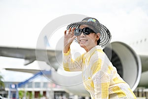 An attractive senior Asian lady in a summer outfit stands at the airport