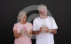 Attractive senior couple smiling using mobile phones. Elderly retiree enjoying social and tech.  Black background