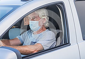 Attractive senior man driving his silver car wearing medical mask due to coronavirus happy for end lockdown at home