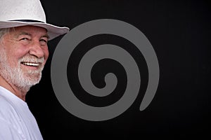 Attractive senior man with white hat and t-shirt looking at camera smiling. Portrait of elderly retired white-haired and beard.