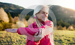 Attractive senior woman doing exercise outdoors in nature, stretching.