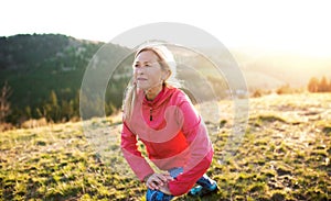 Attractive senior woman doing exercise outdoors in nature at sunset.