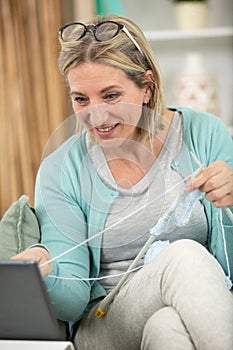 attractive senior woman knitting while using digital tablet