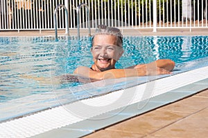 Attractive senior woman relaxing outdoors in the swimming pool enjoying sun and vacation. Elderly woman swimming alone in the blue