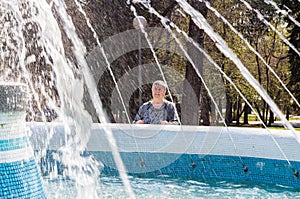 attractive senior woman sincerely smiles standing by fountain. sun rays illuminate woman