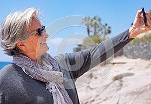 Attractive senior woman white-haired taking selfie at the sea smiling happy. Joyful lifestyles concept, happy retirement
