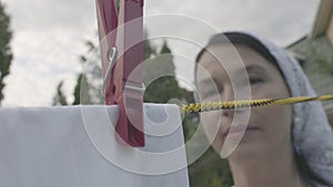 Attractive senior woman with a white shawl on her head hanging white clothes on a clothesline using clothespin outdoors