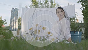 Attractive senior woman with a white shawl on her head resting in the garden sitting on the grass in front of the