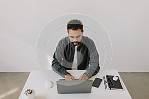 Attractive serious black skinned man in eyeglasses in grey shirt working laptop