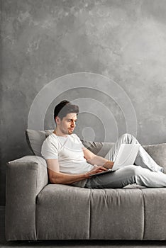 Attractive serious man 30s in basic clothing using laptop, while