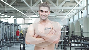 Attractive shirtless blond male bodybuilder in shorts indoors in dark gym, showing muscular torso and ripped abs