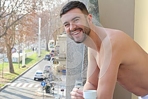 Attractive shirtless man drinking a coffee in the balcony