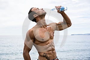 Attractive shirtless muscleman pouring water on his chest from plastic bottle photo