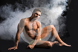 Attractive shirtless muscular man sitting on the floor in swimming suit