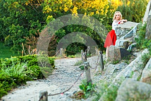 Attractive shoeless happy young blonde woman in stylish red white dress posing on path at hill. standing on road village and