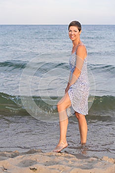 Attractive short haired woman in her thirties wear in light summer dress walks barefoot on the beach with sea in the