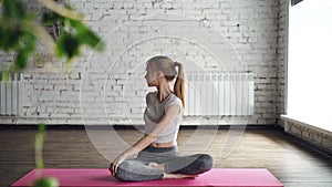 Attractive slim blonde is practicing yoga doing twist poses, bending to side then relaxing in lotus position with hands