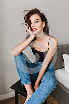 Attractive slim girl with light hairstyle chilling in modern apartment. Fashionable young woman in blue jeans, black T