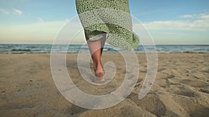 Attractive slim legs of a woman in slow motion walking barefoot along the beach in the early morning. Tourist in a light