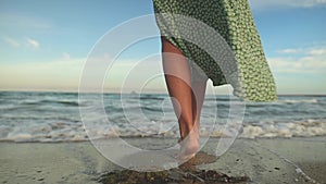Attractive slim legs of a woman in slow motion walking barefoot along the beach in the early morning. Tourist in a light