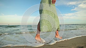 Attractive slim legs of a woman in slow motion walking barefoot along the beach in the early morning. Tourist in a light