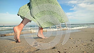 Attractive slim legs of a woman in slow motion walking barefoot along the beach in the early morning. Tourist in a light