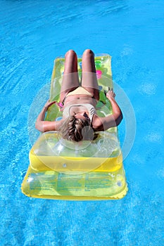 Attractive, slim young lady lying on inflatable sunbed on swimming pool