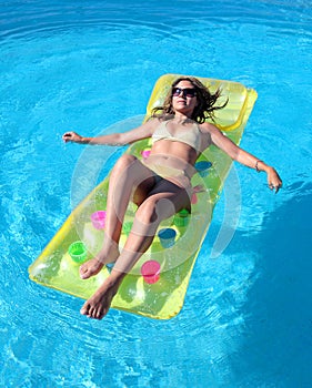 Attractive, slim young lady lying on inflatable sunbed on swimming pool