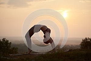 Attractive slim young woman doing yoga exercises outdoors on copy space background of beautiful sky.