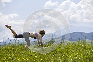 Attractive slim young woman doing yoga exercises outdoors on copy space background of mountains