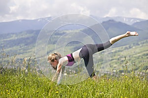 Attractive slim young woman doing yoga exercises outdoors on copy space background of mountains