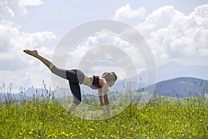 Attractive slim young woman doing yoga exercises outdoors on copy space background of mountains