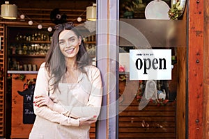 Attractive small business owner businesswoman standing with arms crossed at cafe door and waiting for guests