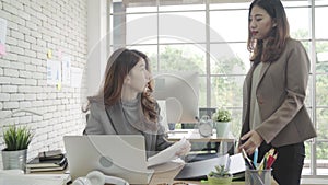 Attractive smart Asian business woman in smart casual wear working on laptop while sitting on desk while her angry manager.