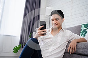 Attractive smart young man sitting on a floor in the living room, using mobile phone