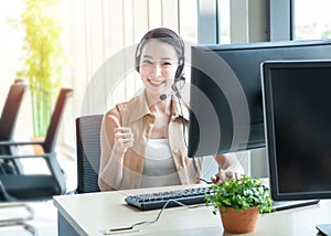 Attractive and smile young asian customer servicer woman wearing headset in modern creative meeting working office sit at computer